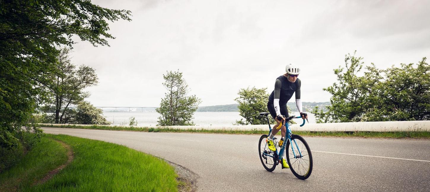 Road cyclists are heading up Munkebjergbakken. The Vejlefjord Bridge is visible in the background.