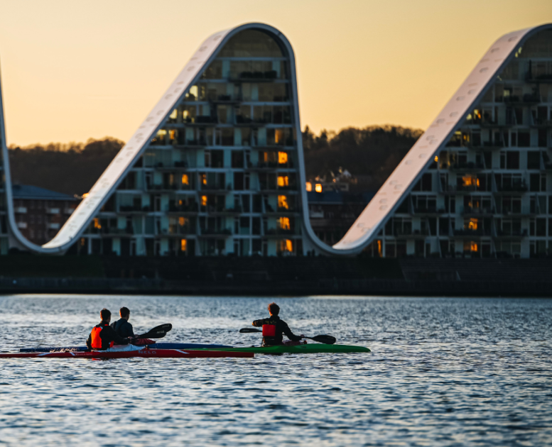 People in kayaks on Vejle Fjord with Bølgen (the Wave) in the background
